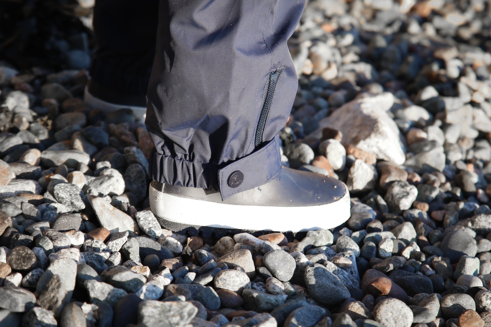Child wearing KidORCA hard-shell waterproof rain pants splashing in a puddle