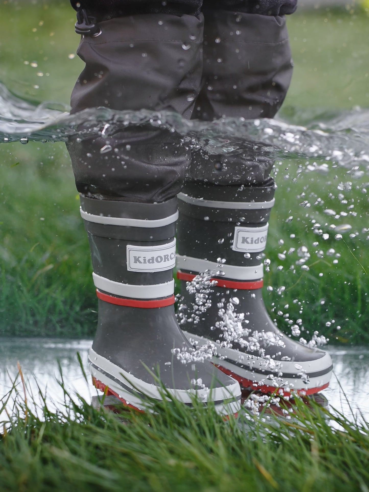 Child splashing in grey rain boots with above-knee waders by KidORCA