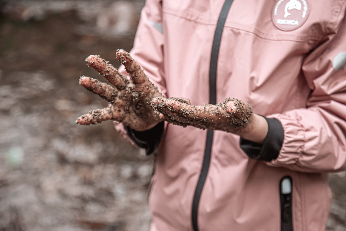 Child playing in rain wearing ash‑rose hard-shell jacket by KidORCA