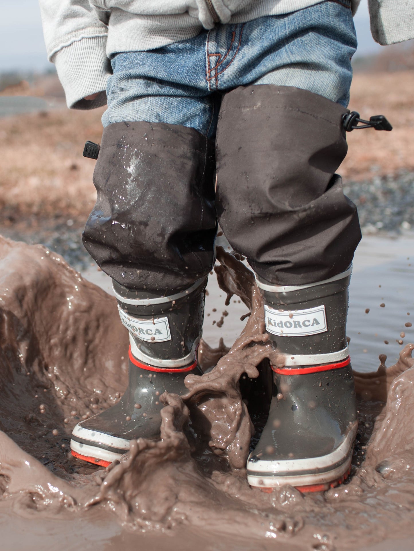 Child splashing in grey rain boots with above-knee waders by KidORCA