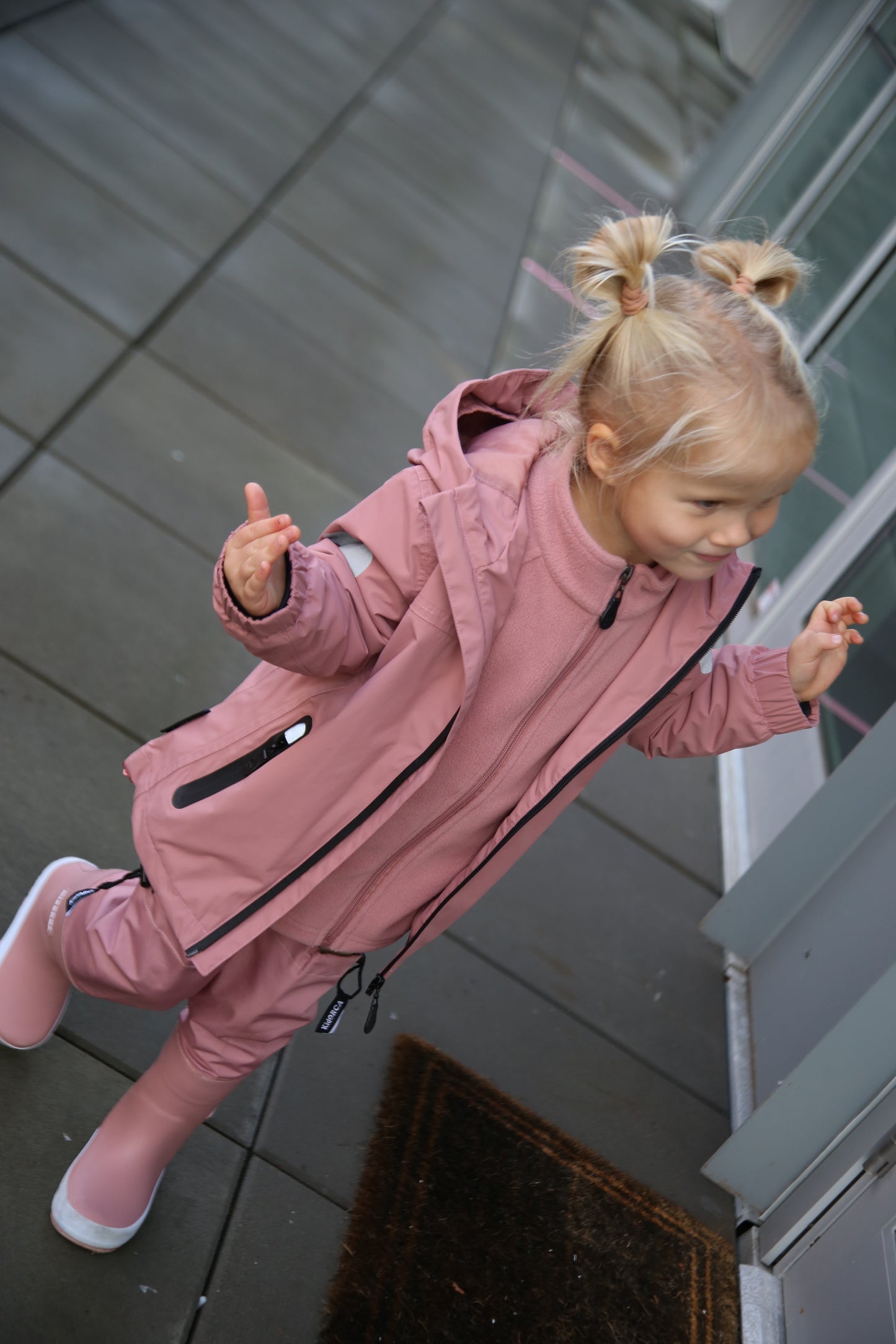 Child playing in rain wearing ash‑rose hard-shell jacket by KidORCA