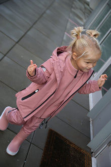 Child playing in rain wearing ash‑rose hard-shell jacket by KidORCA
